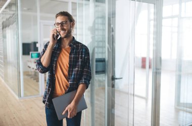 Aramak için cep telefonu teknolojisini kullanan mutlu programcı, bilgisayarlı neşeli erkek blogcu serbest kumanda çalışmasını tartışmak için akıllı telefon konuşması yapıyor