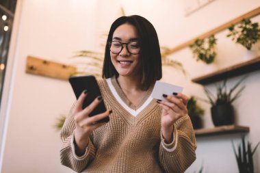 Kartviziti olan Asyalı bir kız kafede akıllı telefondan izliyor. Bin yıllık gülümseyen esmer bir kadının kırpılmış görüntüsü. Dinlenmek, boş zaman ve boş zaman kavramı. Modern kadın yaşam tarzı
