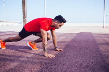 Spor giyim sektöründe genç beyaz bir adam şehrin kenar mahallelerinde sabah antrenmanı sırasında dayanıklı bir şekilde esneme egzersizleri yapıyor. Güçlü bir koşucu koşuya çıkmadan önce ısınıyor.