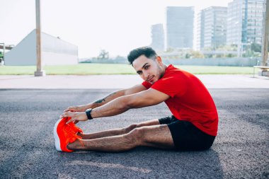 Kafkas fitness antrenörünün kuvvet portresi bacaklarını esneten ve sabah antrenmanında kameraya bakan rahat spor giyim vücut esnekliğiyle genç kaslı bir sporcu.