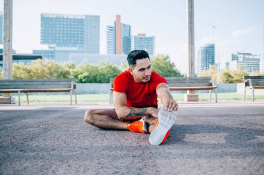 Yakışıklı, güçlü erkek koşucu. Kardiyo antrenmanı yapmak için bacaklarını esnetiyor. Açık havada spor yapıyor.