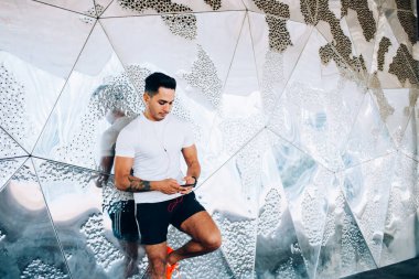 Spor giyim sektöründe beyaz bir adam cep telefonunda kablosuz 4g internet kullanarak spor bloguna bilgi paylaşmak için kardiyo alıştırmaları hakkında yayın yapıyor, kulaklıklı erkek koşucu dinlemek için medyayı seçiyor