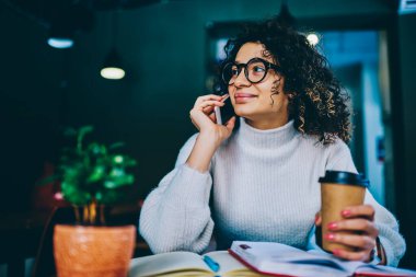 Orta Doğulu bir öğrenci elinde kahve fincanı ile modern cep telefonu cihazıyla danışmanlık konuşması yapıyor. Kapalı mekanlarda 4G kablosuz ağ kullanıyor. Cep telefonu uygulaması aracılığıyla ders kitaplarıyla arayan zeki bir blogcu.