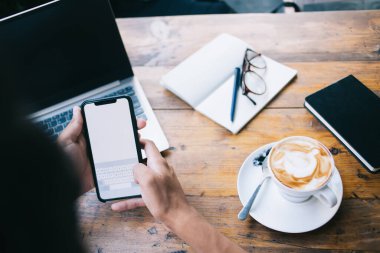 Seçici odak noktası modern akıllı telefon teknolojisini kullanarak 4G kablosuz internet mesajlaşmasını kullanarak kafeterya masasında kapuçino içeceği ve dijital cihazlarla oturan erkek eli.