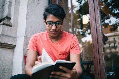 Göz düzeltmesi için moda gözlüklü zeki erkek öğrenci eğitimde bilgilendirici yayınlar en çok satan kitaplar şehirdeki entrikaları analiz eden gözlüklü Latin hippi adam ders kitabı tutuyor.