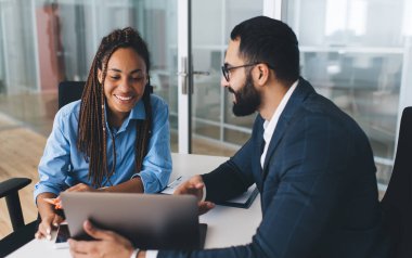 Başarılı iş adamları ofis içi dizüstü bilgisayarlarını kullanarak şirket web sitesinde metin bilgilerine göz atıyorlar, yetenekli erkek ve kadın çalışanlar online rezervasyon yaparken uygulamayı tartışıyorlar