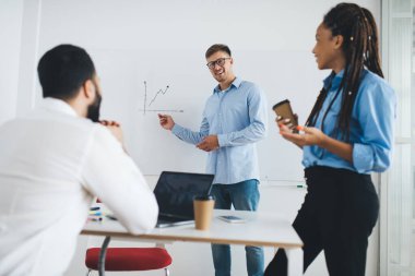 Ofiste beyin fırtınası sırasında iş pazarlamasını tartışan çeşitli erkek ve kadın meslektaşlar, toplantı odasındaki bilgi grafiklerini açıklayan gözlüklü mutlu profesyonel çalışan