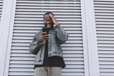 Optik gözlüklü heyecanlı erkek cep telefonu teknolojisini kullanarak iyi haberlere şaşırdı, hipster adam mobil uygulama üzerinden seyahat rezervasyonu yaptığı için indirim aldı.