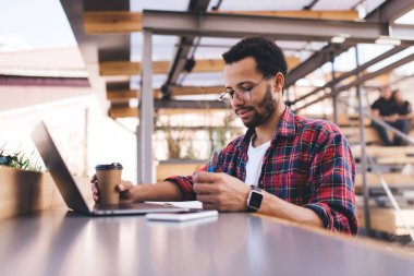 Klasik gözlüklü yetenekli erkek öğrenci, dizüstü bilgisayar başında oturup bilgisayar başında ders kitabı notlarını analiz ederek ve proje için milenyum insan planlama organizasyonunu izleyerek günlerini geçiriyor.