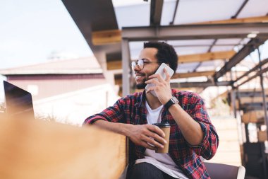 Optik gözlüklü neşeli erkek göz düzeltmesi yapıyor. Konuşurken mobil iletişimin keyfini çıkarıyor. Kahve alıp sohbet etmek için cep telefonu kullanan İspanyol hippi adam.