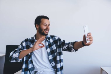 Neşeli erkek kişi cep telefonunun ön kamerasında fotoğraf çekerken iyi görünüyor, mutlu milenyum blogcusu gülümserken akıllı telefon uygulaması üzerinden selfie etkisi yapıyor.