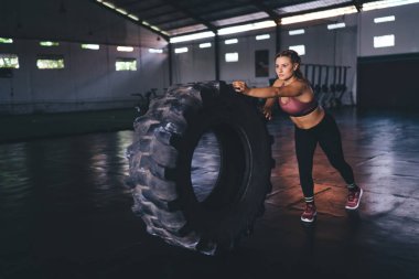 20 yaşında çekici bir kadın spor salonunda spor yaparken antrenman ekipmanlarıyla çalışıyor. Spor salonunun içinde tekerlek lastiği ağırlık kaldıran beyaz bir bayan sporcu.