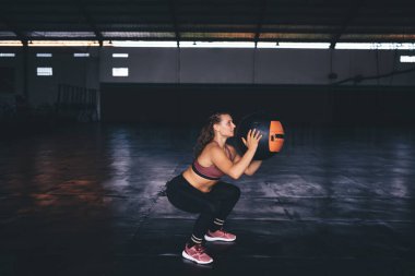 Aktif giyimli beyaz kadın, formda kalmak için sabah antrenmanlarında çömelme egzersizleri yapıyor. Spor topu ekipmanlarıyla antrenman yaparken zayıf vücutlu, kaslı ve kaslı bir kadın.