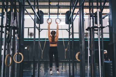 Spor giyimli genç bir kadın spor jimnastik yüzükleriyle egzersiz yapıyor spor salonunun içinde egzersiz yapıyor spor malzemeleriyle vücut geliştirme eğitimine arka planda katılıyor.