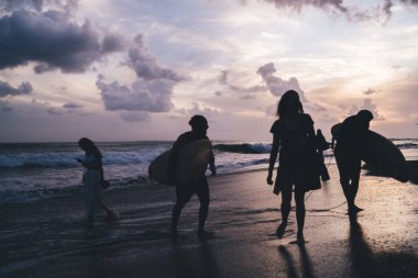 Gece deniz kıyısında elinde sörf tahtaları olan genç insanların siluet görüntüsü, tanınmayan erkek ve kadın sörfçülerin okyanus kenarında iletişim kurmaları - yaz tatilleri