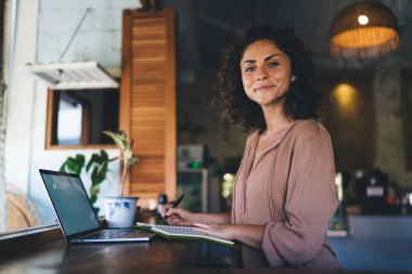 Eğitimde ders kitabı ve modern dizüstü bilgisayarı olan ve e-öğrenim ve bilgilendirici araştırmalar için kameraya bakan kız öğrencinin portresi, dijital netbook pozu veren yetenekli hippi kız.