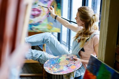 Paleti olan beyaz kadın sanatçı resim sehpasında resim çizerek resim yapıyor. Sanat galerisinde Windosill 'de dinleniyor. Yetenekli kadın sanat tutkusuna ve ilham kaynağına sahip.