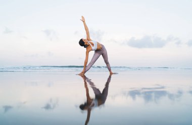 Spor eşofmanlı bir kadın sahilde pilates yaparken egzersiz yapıyor, Kafkasyalı formda bir kız yoga sırasında esnerken sağlıklı yaşam tarzına ve sağlığına kavuşuyor.
