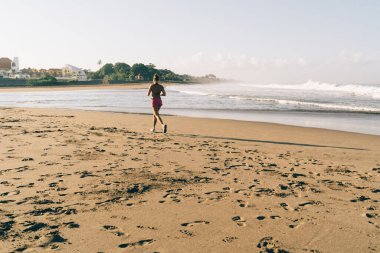 Deniz kıyısında sabah tatillerinde koşan sportif bir kadın, sağlıklı yaşam tarzının ve canlılığın tadını çıkaran zayıf zinde bir kız mükemmel vücut ve vücut yapısını korumak için sahil şeridinde koşuyor.