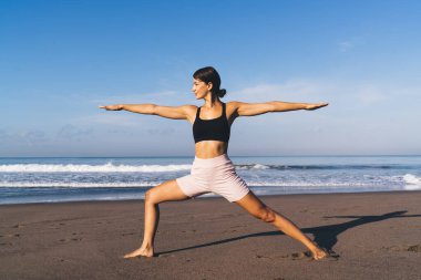 Aktif halde olan esnek beyaz kadın sabah yogası sırasında egzersiz yapıyor canlılık ve ahenk hissediyor, genç zayıf kadın deniz kıyısındaki antrenman sırasında vücudunu esnettiği için asana yapıyor.