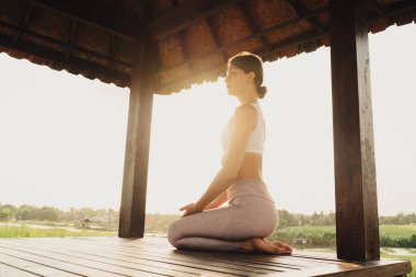 Spor giyim sektöründe sakin bir kadının sabah güneşini Endonezya 'daki hatha yoga pratiği sırasında meditasyon için harcadığı beyaz kadın Vietnam' da uyum içinde inzivaya çekilirken bütünsel iyileşmenin keyfini çıkarıyor.