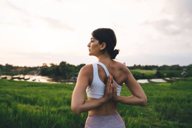 Beyaz bluzlu beyaz elbiseli genç bir kadının namaste 'de el ele tutuşması ve pirinç tarlalarındaki bütünsel iyileşme sırasında iç huzuru ve farkındalığı düşünmesi.