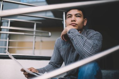 Asyalı milenyum adamı bir şeyler düşünür ve ofis binasının yanındaki merdivenlere bakar. Dinlenme ve işten ayrılma kavramı. Modern, başarılı bir adamın fikri. Gazetesi olan genç bir erkek. Güneşli bir gün