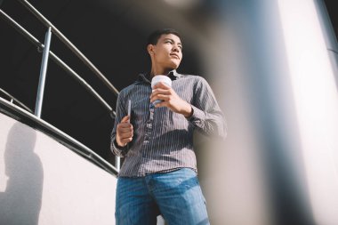 Bin yıllık bilgisayarlı ve kahveli bir adamın ofis binasının yakınındaki merdivenlere bakışının alt görüntüsü. Dinlenme ve işten ayrılma kavramı. Modern, başarılı bir adamın fikri. Genç Asyalı erkek. Güneşli bir gün