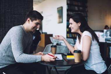 Masada oturmuş gülerken ve el kol hareketi yaparken finansal ayrıntıları tartışan neşeli iş arkadaşlarının yan görüntüsü