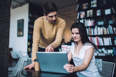 Çağdaş çalışma alanındaki kadın meslektaşlarına iş stratejisini açıklarken, günlük giysiler içindeki ciddi genç erkek çalışanlar dizüstü bilgisayara işaret ediyorlar.