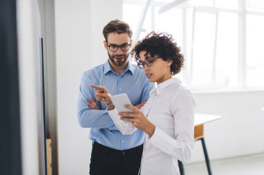 İş kadını akıllı telefondan izliyor ve interaktif tahtayı erkek arkadaşına işaret ediyor. İş birliği ve takım çalışması kavramı. Genç Avrupalı milenyum meslektaşları görevde