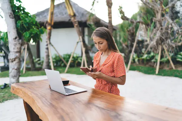 Stock image Caucaisan female using cellphone device for sharing media files to laptop computer connecting to 4g wireless and bluetooth outdoors, millennial graphic designer with netbook chatting via mobile app