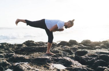 Spor giysilerinde çıplak ayaklı erkek yogi kayalık sahil şeridinde spor yapıyor sağlıklı yaşam tarzını koruyor, beyaz adam yoga pozisyonunda, uyum için meditasyon yapıyor barış dinlenmeye odaklanıyor.