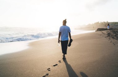 Hafta sonu boyunca deniz kıyılarında esnemek ve yürümek için elinde bir şişe su ve hasırla gezen sportif adamın arka görüntüsü, Kafkas erkek yogi 'nin kumlu sahil şeridinde boş vakitlerini geçirmesi