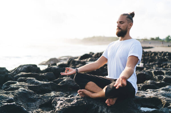 Harmony and meditation training during morning yoga at coastline with rocks, Caucaisan male in sportswear sitting in lotus pose during hatha practice for exercising body concentration in asana
