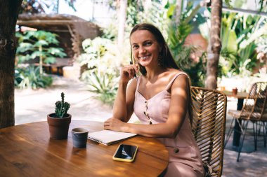 Not defteriyle sokak kafesinde poz vermeyi planlayan neşeli yetenekli öğrencinin yarım boy portresi. Not defteri olan başarılı hippi kız kameraya gülümserken ödev yapıyor.