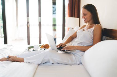 İpek gecelikli neşeli bir kadın dizüstü bilgisayarla otel odası servisini online olarak rezerve ediyor. Hafta sonunun tadını çıkartıyor. Kafkasyalı dijital göçebe ağ ağlarında sohbet ediyor.