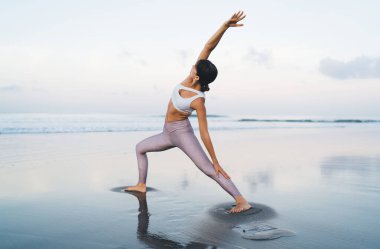 Spor eşofmanlı bir kadın sahilde pilates yaparken egzersiz yapıyor, Kafkasyalı formda bir kız yoga sırasında esnerken sağlıklı yaşam tarzına ve sağlığına kavuşuyor.