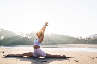 Eşofman giymiş esnek beyaz kadın vücut kaslarını çalıştırmak için sicim egzersizi yapıyor. Spor yapan 20 yaşındaki kadın sabah yogası yaparken sahil şeridinde yoga yapıyor.