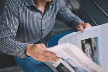 Merdivenlerde gazete okuyan bin yıllık bir adamın kırpılmış görüntüsü. Dinlenme ve işten ayrılma kavramı. Modern, başarılı bir adamın fikri. Gömlek ve kot giyen bir erkek. Güneşli bir gün