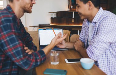 Ofiste dizüstü bilgisayarla konuşan ve çalışan çok ırklı iş adamlarının görüntüsü. İş birliği ve takım çalışması kavramı. Modern başarılı adamlar. Masadaki genç Asyalı ve beyaz adamlar.