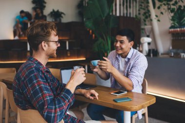 Ofisteki masada konuşan ve içki içen çok ırklı iş adamları. Dinlenme ve işten ayrılma kavramı. Modern başarılı adamlar. Genç, gülümseyen Asyalı ve Kafkasyalı adamlar birbirlerine bakıyorlar.