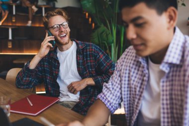 Asyalı iş arkadaşı cep telefonu kullanırken beyaz iş adamı akıllı telefondan konuşuyor. İş birliği ve takım çalışması. Modern başarılı adamlar. Ofisteki masada çalışan gençler.