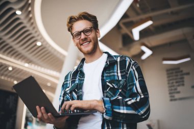 Kafkasyalı adamın dizüstü bilgisayar kullanıp ofis alanındaki kameraya baktığı son görüntü. Esnek iş yeri kavramı. Serbest çalışma ve uzaktan kumanda fikri. Genç, gülümseyen sakallı, gözlüklü başarılı adam.