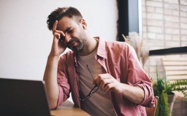 Elektronik kulaklıklar takan Kafkasyalı bilişim uzmanı, son teslim tarihi sırasında baş ağrısı hissediyor. Kafenin içinde çalışıyor, yorgun erkek programcı dizüstü bilgisayarlı, fazla mesai sırasında ses kitabı dinliyor.