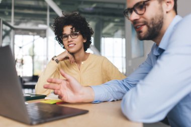 İş adamı, iş arkadaşı kameraya bakarken dizüstü bilgisayardan bir şey izliyor. İş birliği ve takım çalışması. Avrupalı bin yıllık meslektaşlar masada. Modern başarılı insanlar