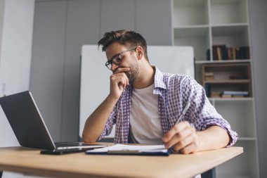 Milenyum Kafkas işadamı panoya bir şeyler yazarken bir şeyler düşünüyor. Modern başarılı adam kavramı. Gözlüklü, gözleri kapalı genç adam açık uzay ofisinde masada oturuyor.
