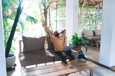 Kafkas dijital göçebe, modern laptop teknolojisiyle açık hava iş yerinde dinleniyor ve esniyor, netbook bilgisayarlı genç erkek programcı uzaktan çalışma molasına sahip.