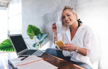 Modern cep telefonlu mutlu kız öğrenci kameraya gülümsüyor e-maket bilgisayarında fotokopi alanı, cep telefonu ve netbook ile neşeli blog yazarının portresi oluşturuluyor.