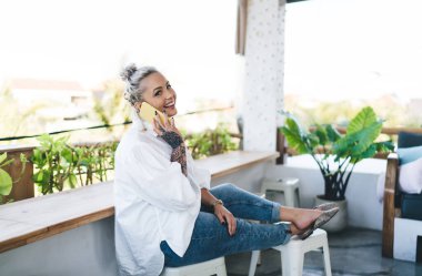 Yüzünde sevimli bir gülümseme olan neşeli bir kadın, hafta sonu sokak kafesinde uluslararası akıllı telefon görüşmesi yaparken eğleniyor, en iyi arkadaşıyla gezmek ve konuşmak için gezen mutlu kadın portresi kullanıyor.